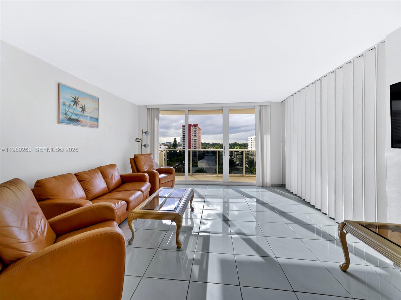 A living room features tan leather furniture, white tile floors, and a balcony with city views — 3140 S Ocean Dr # 612, Hallandale Beach FL 33009, HALLANDALE BEACH, FL
