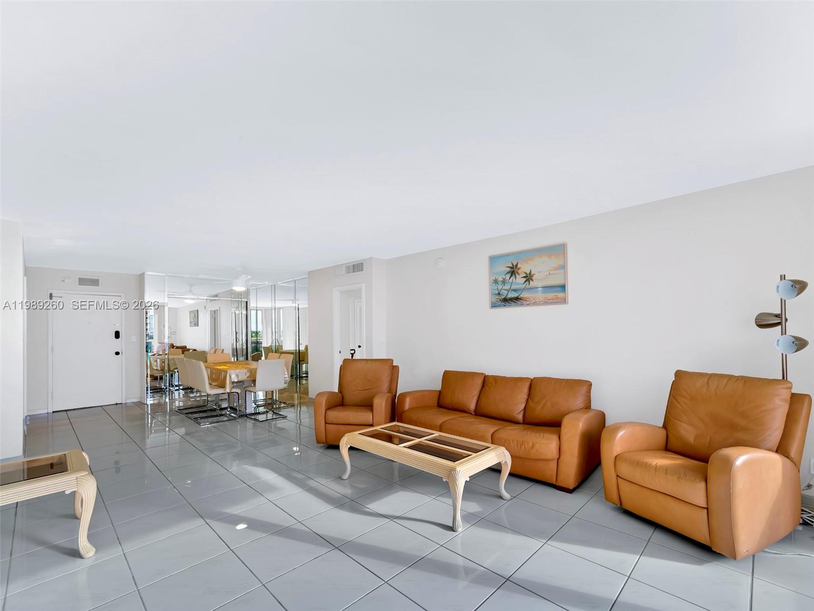 A living room with tan leather furniture, a glass-topped coffee table, and light gray tile flooring — 3140 S Ocean Dr # 612, Hallandale Beach FL 33009, HALLANDALE BEACH, FL