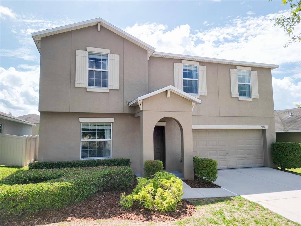 A two-story suburban house with a tan stucco exterior, a garage, and landscaped front yard — 3621 KEARSNEY ABBEY CIRCLE, DOVER, FL