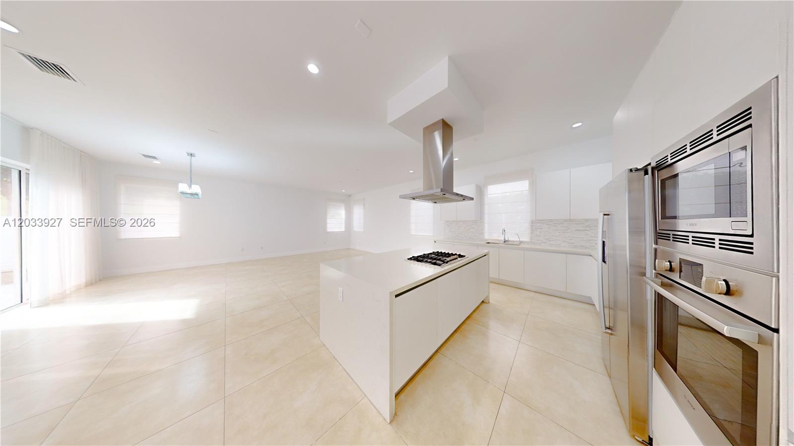 A modern, minimalist kitchen features white cabinetry, a central island with a cooktop, and stainless-steel appliances — 9980 NW 74th Ter # 9980, Doral FL 33178, DORAL, FL