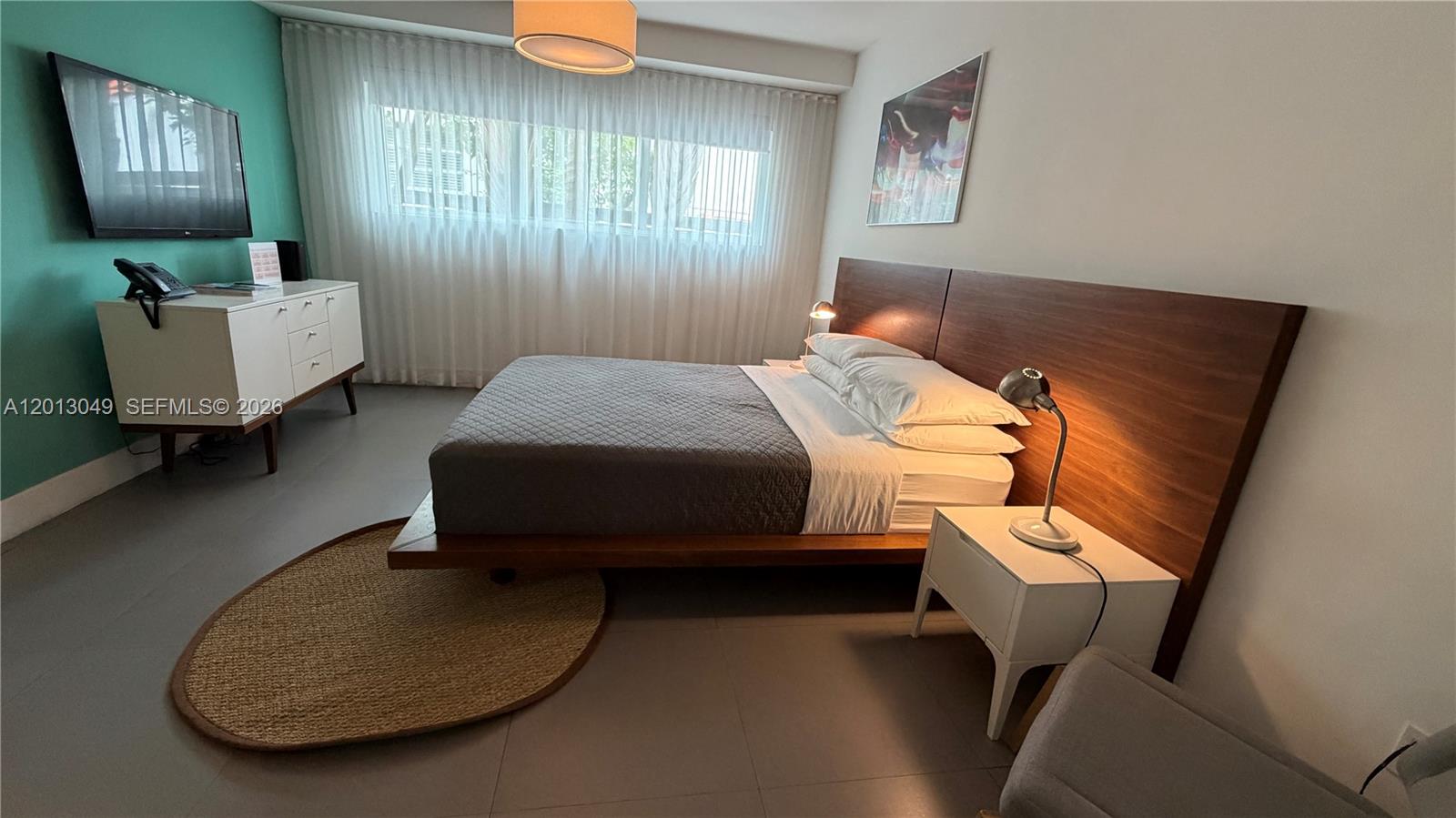 A bedroom features a platform bed with a wood headboard, white furniture, and teal wall — 1816 Meridian Ave # 9, Miami Beach FL 33139, MIAMI BEACH, FL