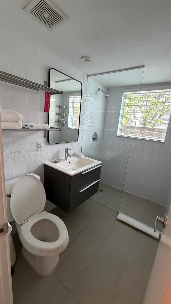 A modern bathroom features a floating vanity, a walk-in glass shower, and white tile walls — 1816 Meridian Ave # 9, Miami Beach FL 33139, MIAMI BEACH, FL