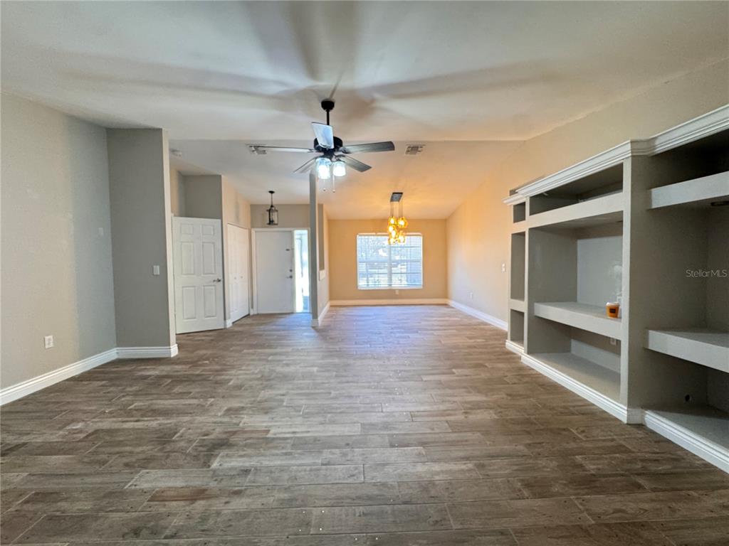 An open-concept living area features wood-look tile flooring, a ceiling fan, and built-in shelving — 5619 COLONIAL OAKS BOULEVARD, SARASOTA, FL