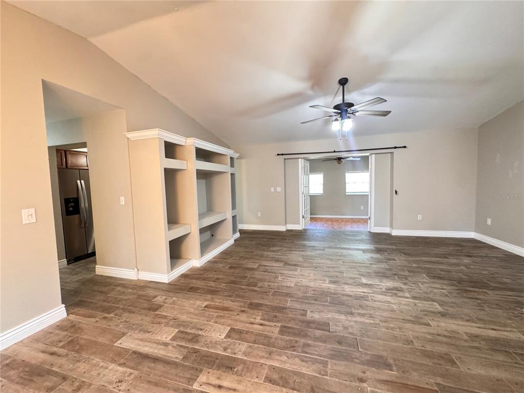 A living room features wood-look tile flooring, a built-in shelving unit, and a ceiling fan — 5619 COLONIAL OAKS BOULEVARD, SARASOTA, FL