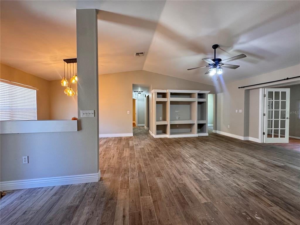 An open living area features wood-look tile flooring, a built-in media center, and vaulted ceilings — 5619 COLONIAL OAKS BOULEVARD, SARASOTA, FL