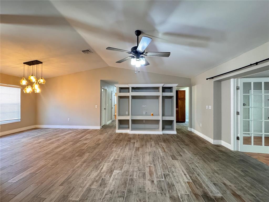 A living room features wood-look tile flooring, a ceiling fan, and a built-in media center — 5619 COLONIAL OAKS BOULEVARD, SARASOTA, FL