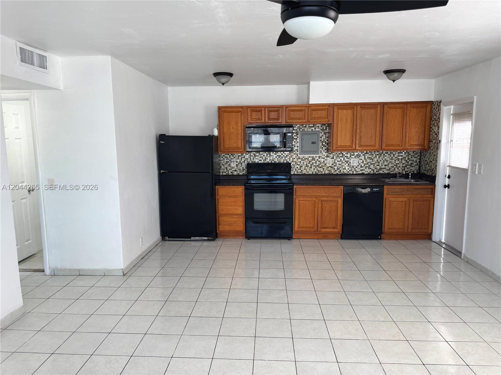 A kitchen features wood cabinets, black appliances, a tiled backsplash, and light-colored floor tiles — 1765 Venice Ln # 4E, North Miami FL 33181, NORTH MIAMI, FL