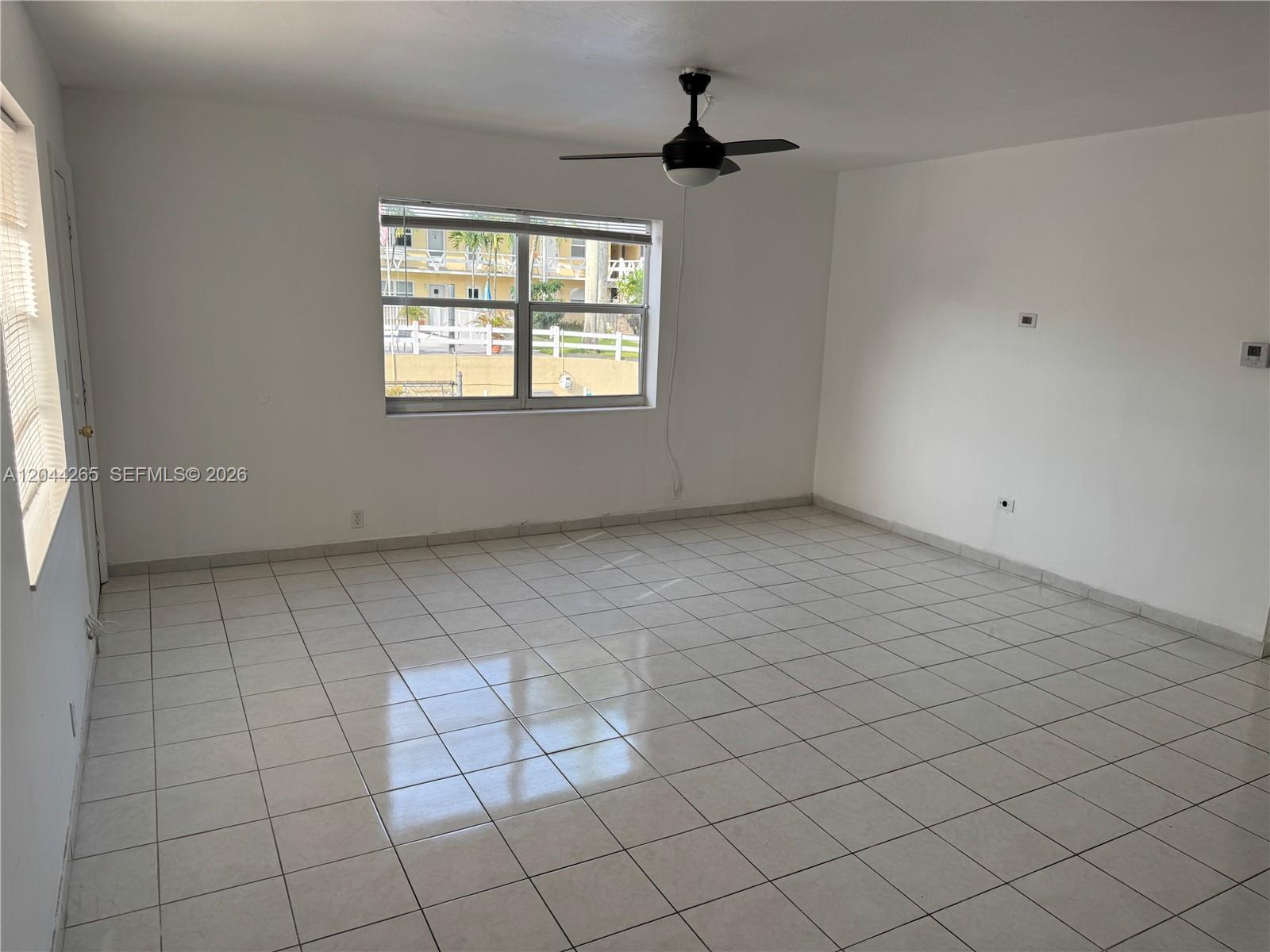 An empty room features white walls, light-colored tile flooring, a ceiling fan, and a window — 1765 Venice Ln # 4E, North Miami FL 33181, NORTH MIAMI, FL