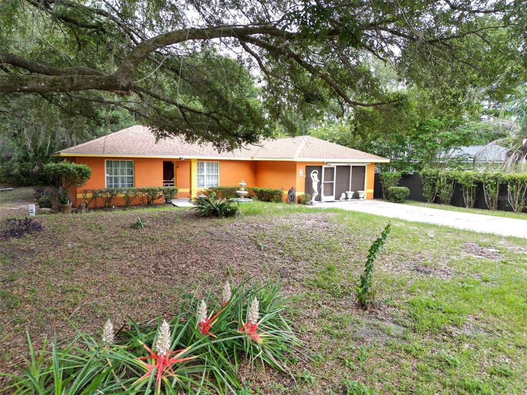 A single-story orange house with a tan roof sits behind a large, grassy front yard — 10 SEQUOIA DRIVE TRACE, OCKLAWAHA, FL