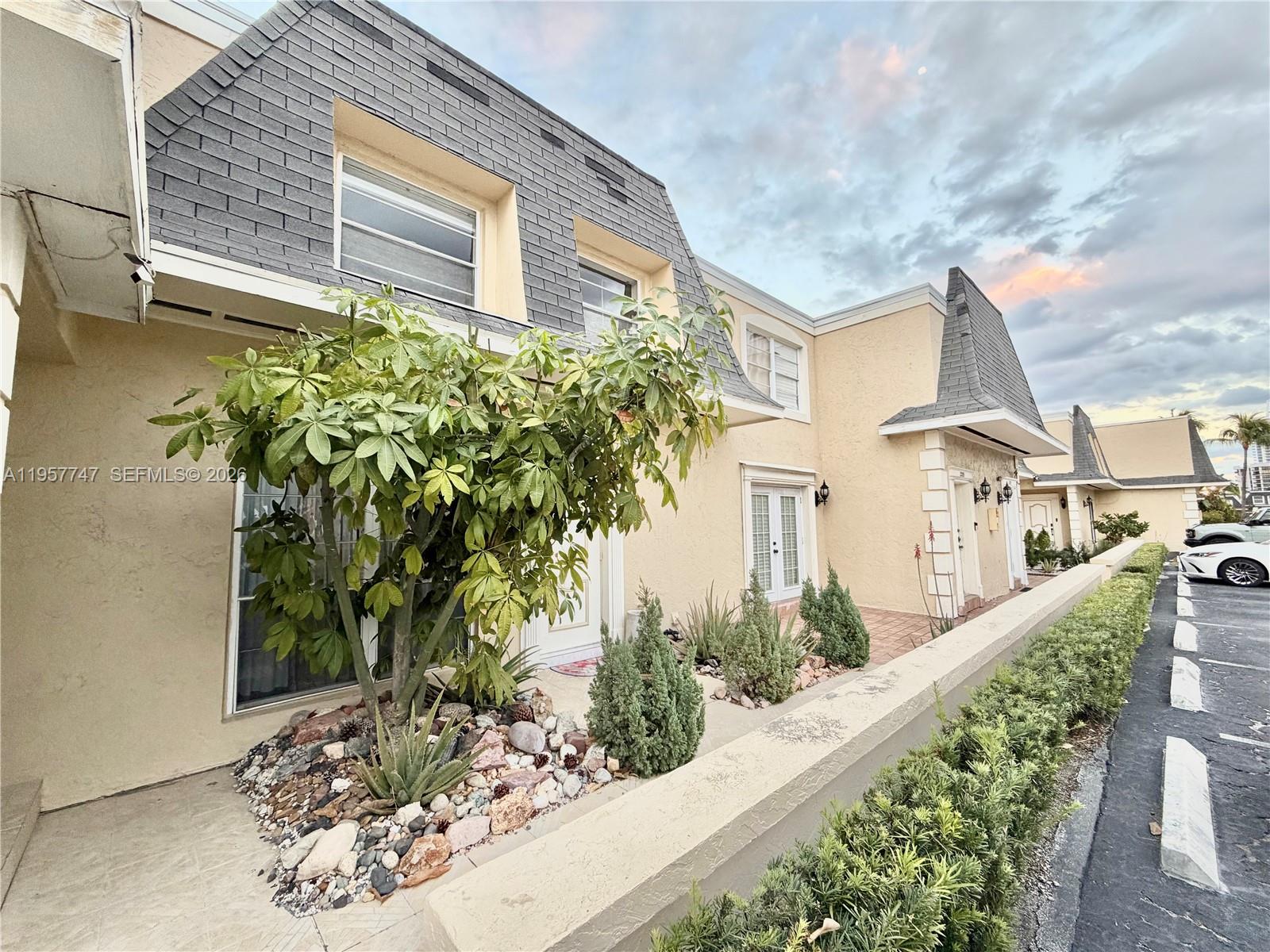 A row of townhouses features mansard roofs, beige stucco walls, and a landscaped front garden — 2203 NE 7th St # 14, Hallandale Beach FL 33009, HALLANDALE BEACH, FL