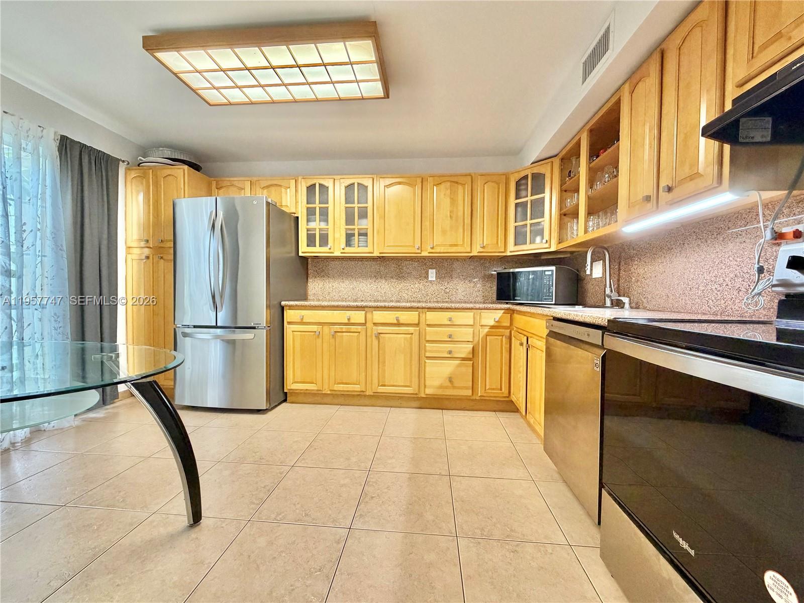 A kitchen features light wood cabinets, stainless steel appliances, and beige tile flooring — 2203 NE 7th St # 14, Hallandale Beach FL 33009, HALLANDALE BEACH, FL