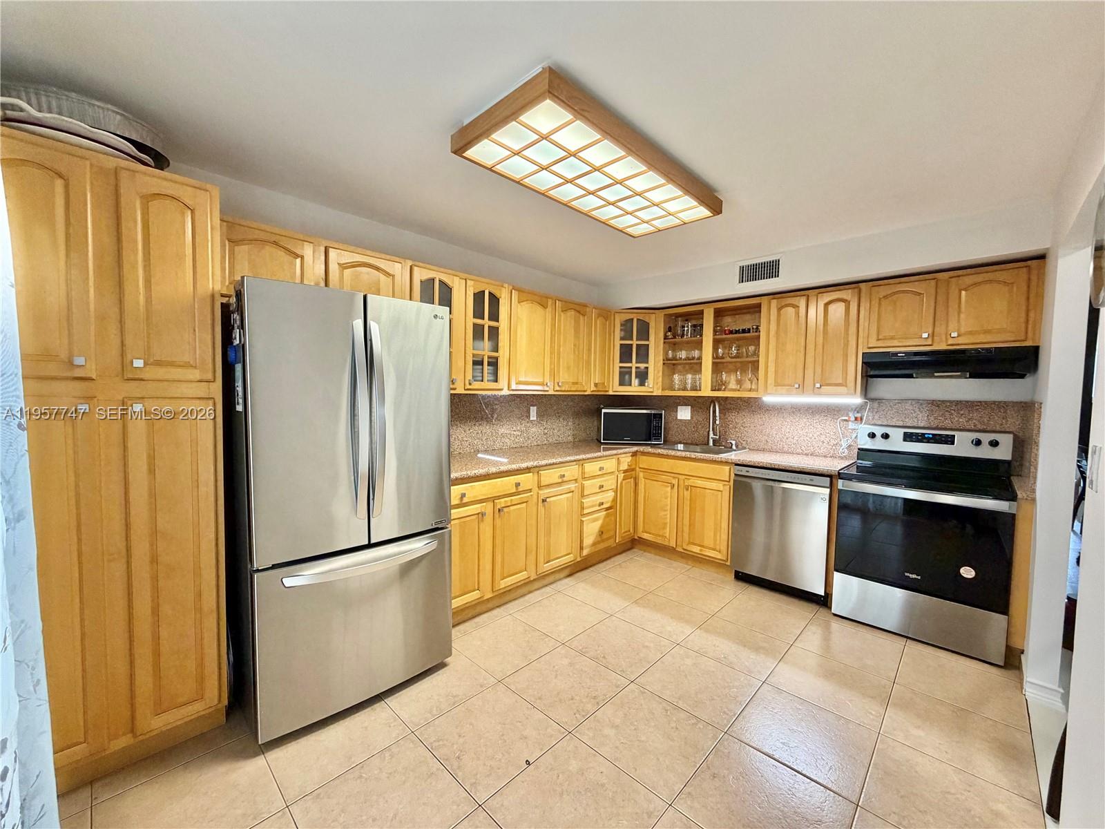 A kitchen features light wood cabinets, stainless steel appliances, and a grid-patterned ceiling light — 2203 NE 7th St # 14, Hallandale Beach FL 33009, HALLANDALE BEACH, FL