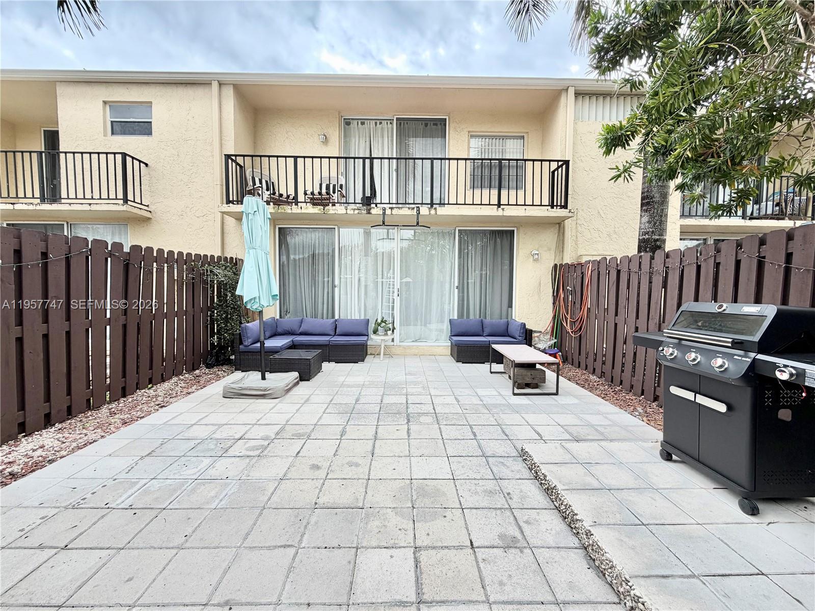 A paved patio features outdoor furniture, a grill, and a fenced backyard with a balcony above — 2203 NE 7th St # 14, Hallandale Beach FL 33009, HALLANDALE BEACH, FL