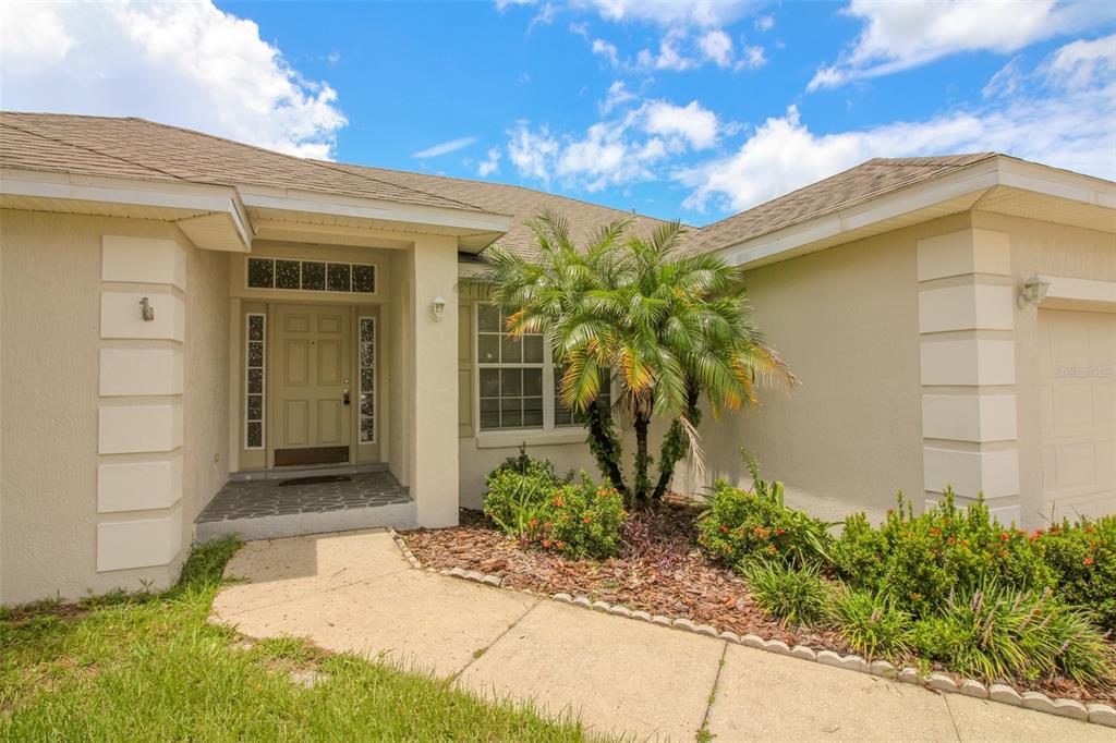 A beige house exterior features a front entrance, a palm tree, and a concrete walkway — 6719 HIGHLANDS CREEK BOULEVARD, LAKELAND, FL