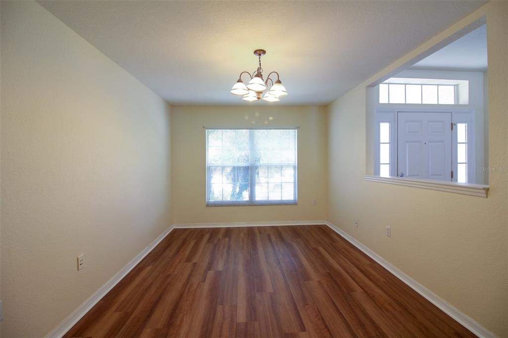 An empty dining room with wood-look flooring, a central chandelier, and a large window — 6719 HIGHLANDS CREEK BOULEVARD, LAKELAND, FL