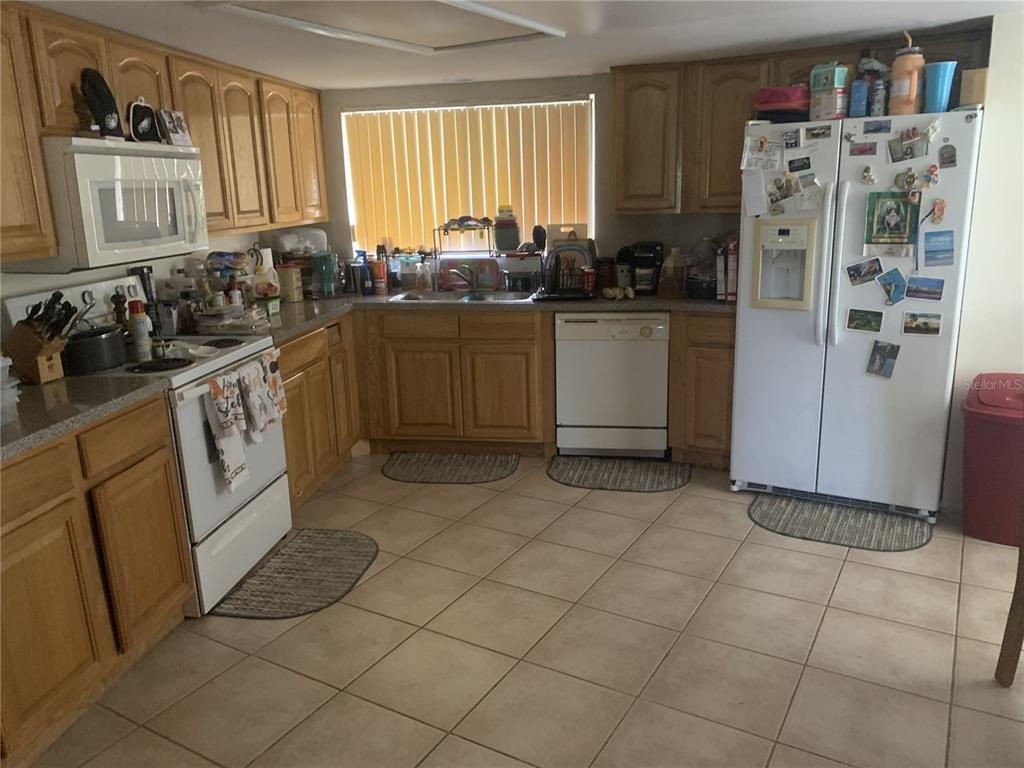 A kitchen features light wood cabinets, white appliances, tile flooring, and a window with blinds — 1064 LOTUS PARKWAY UNIT 915, ALTAMONTE SPRINGS, FL