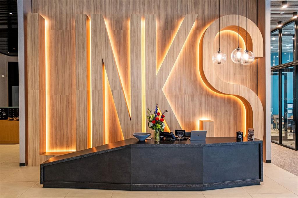 A modern reception desk sits in front of a large, illuminated wooden wall sign reading LINKS — 1991 MAIN STREET UNIT Links B1 PH, SARASOTA, FL