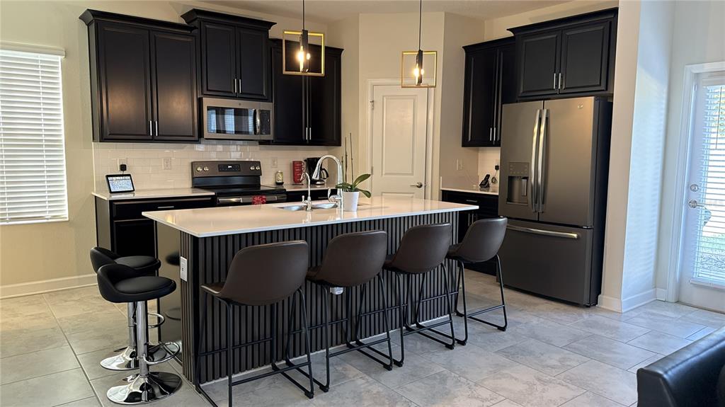 A modern kitchen features black cabinetry, a white-topped island with slat detailing, and stainless appliances — 1055 BLACKWOLF RUN ROAD, DAVENPORT, FL