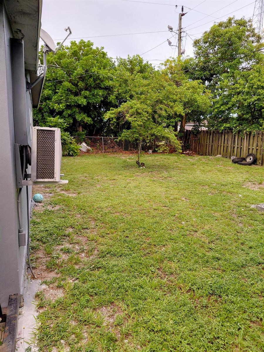 A grassy backyard features a central tree, a wooden fence, and an exterior air conditioning unit — 3210 NW 18th Place, Lauderhill FL 33311, LAUDERHILL, FL