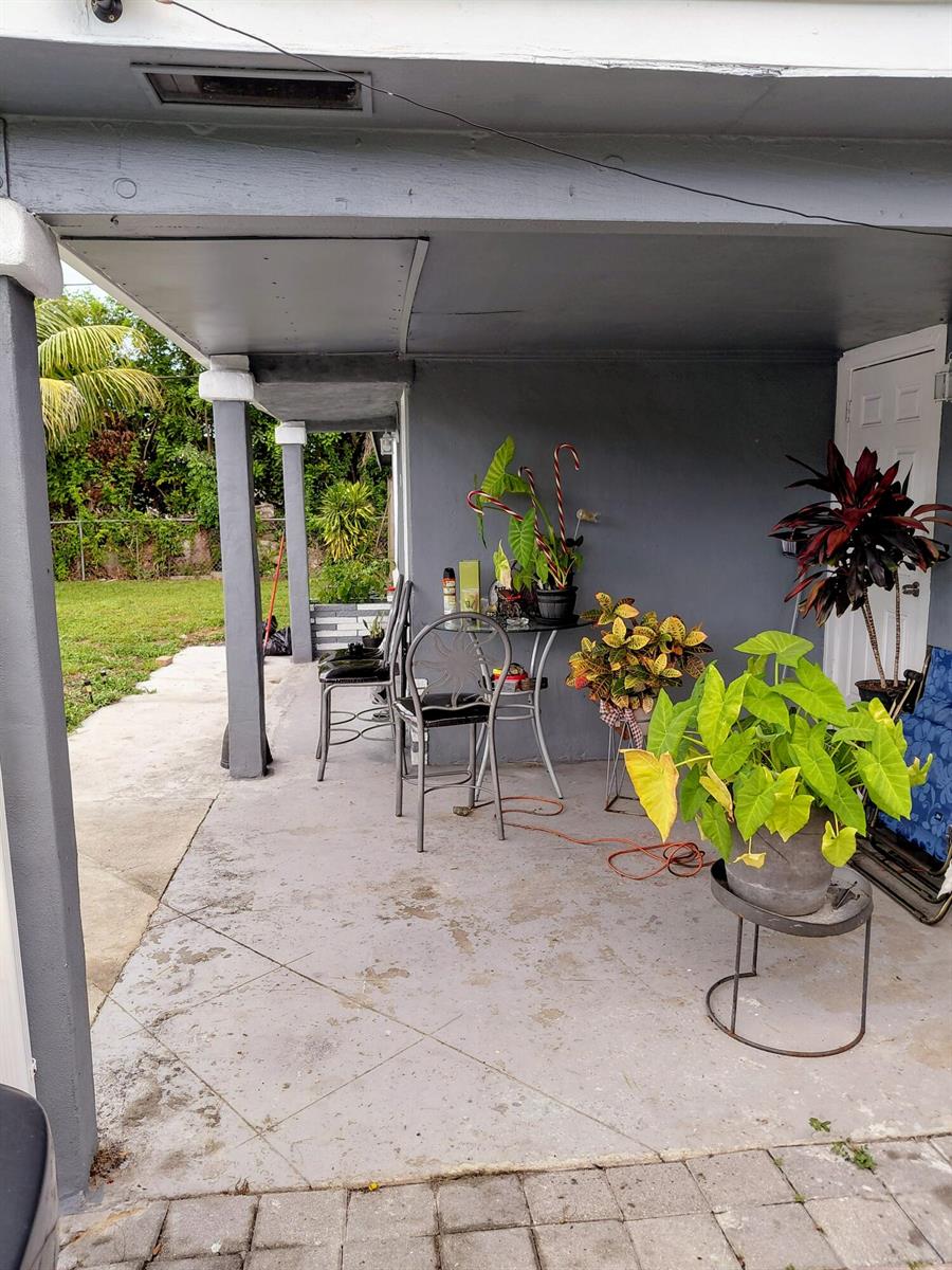 A covered concrete patio features several potted plants, a small table, and two chairs — 3210 NW 18th Place, Lauderhill FL 33311, LAUDERHILL, FL