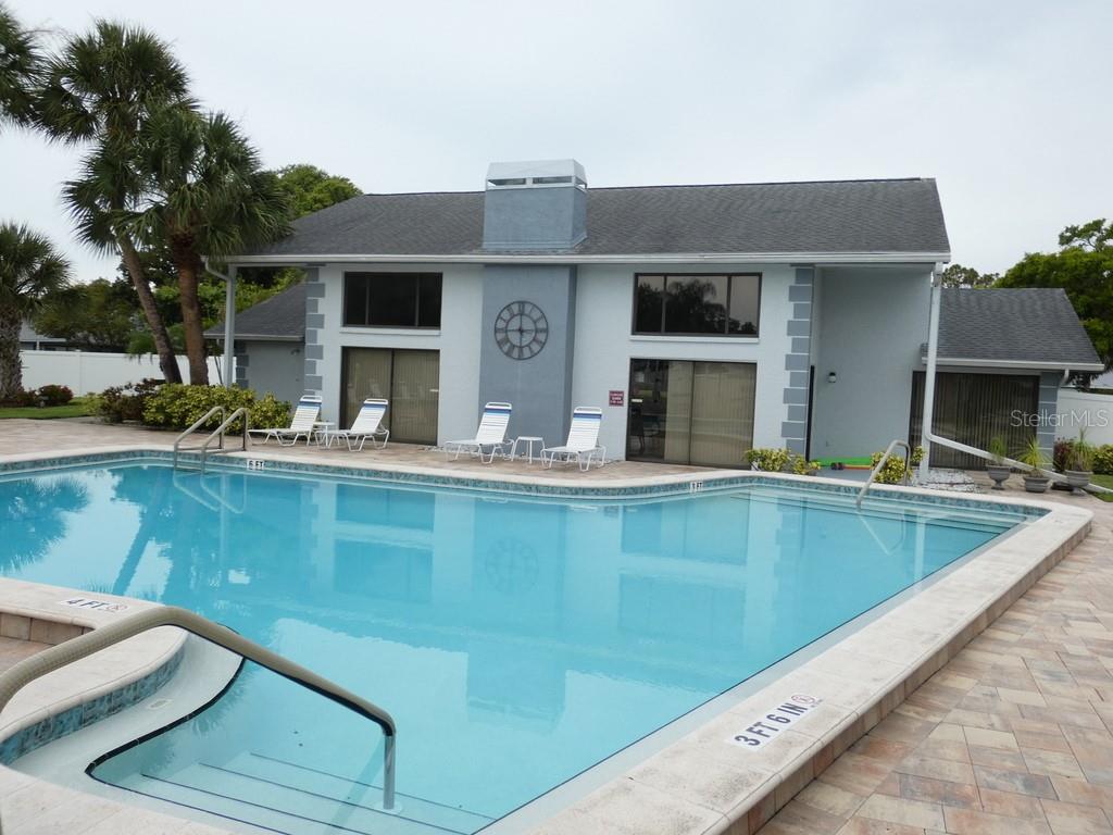 A swimming pool sits in front of a light blue building with a central chimney — 2749 COUNTRYSIDE BOULEVARD UNIT 28, CLEARWATER, FL