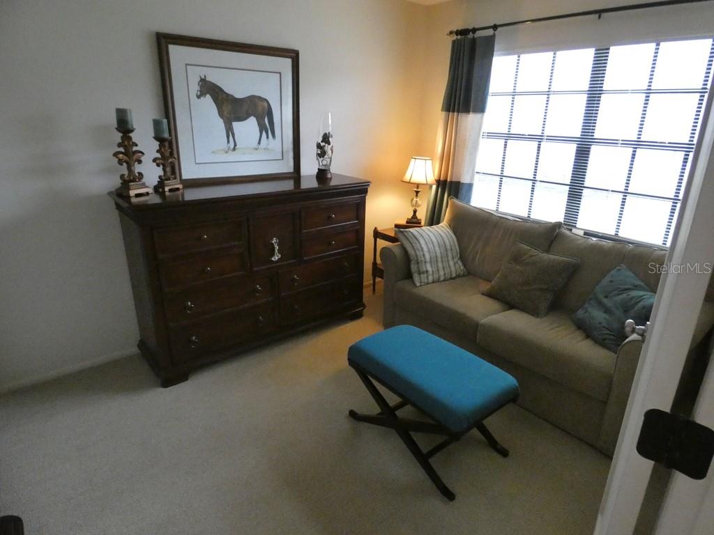 A room features a dark wood dresser, a beige sofa, and a blue ottoman — 2749 COUNTRYSIDE BOULEVARD UNIT 28, CLEARWATER, FL