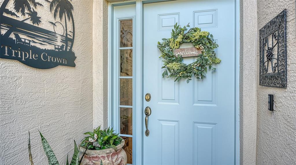 A light blue front door with a wreath and side window sits beside a wall sign — 5811 WHITE OAK BAYOU COURT, BRADENTON, FL