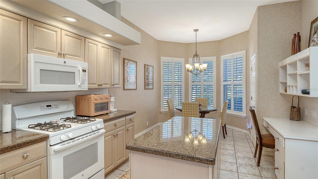 A kitchen with granite countertops, light wood cabinets, a center island, and a dining area — 5811 WHITE OAK BAYOU COURT, BRADENTON, FL