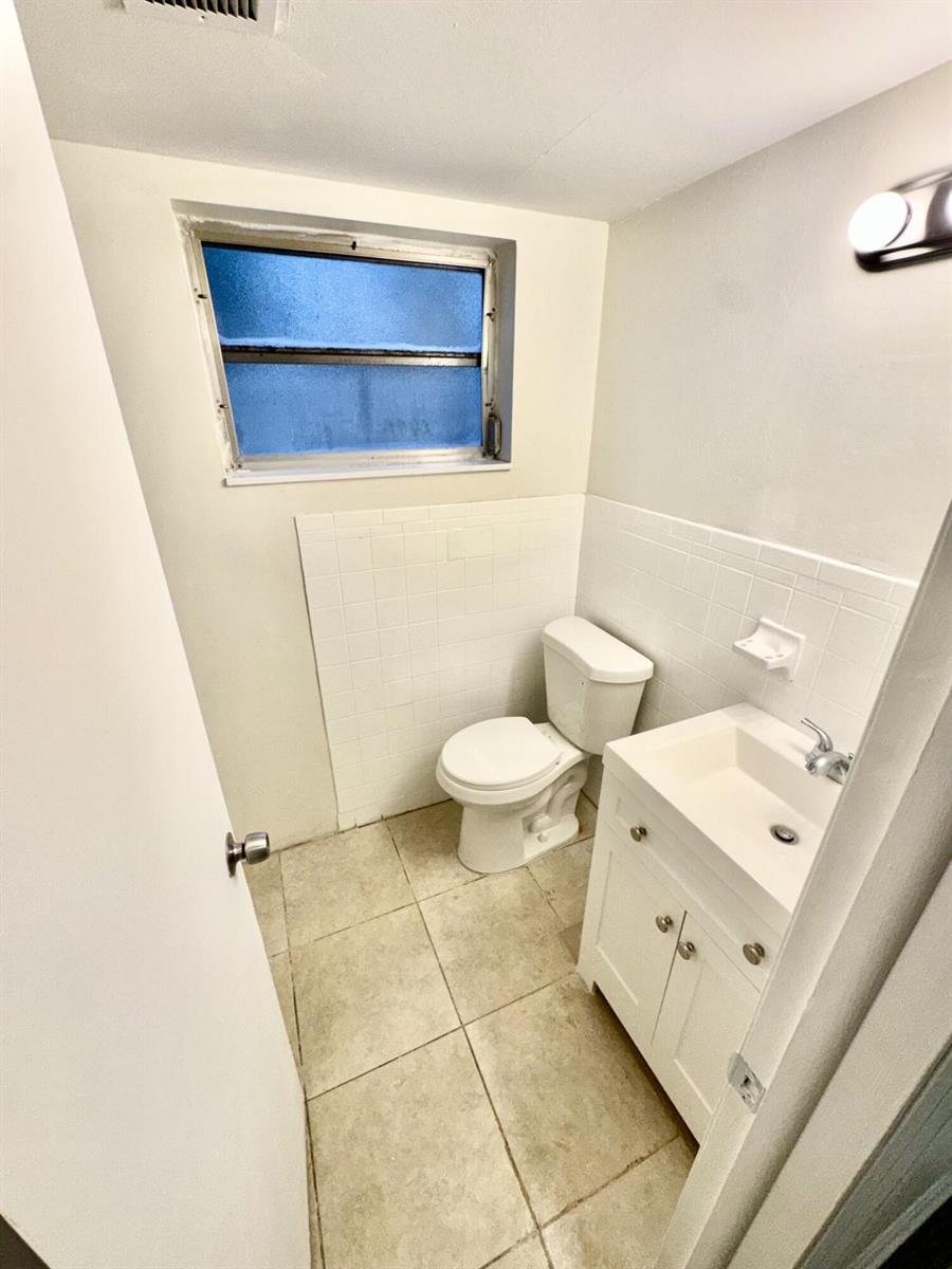 A small bathroom features a white vanity, a toilet, tiled flooring, and a window — 417 N K Street # 1a, FL 33460, FL