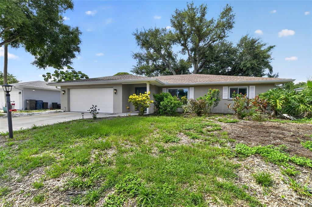 A single-story house with a white garage door, tan exterior, and a large front yard — 7207 14TH AVENUE NW, BRADENTON, FL