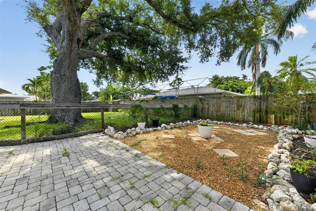 A backyard features a paver patio, a gravel area with stepping stones, and a large tree — 7207 14TH AVENUE NW, BRADENTON, FL