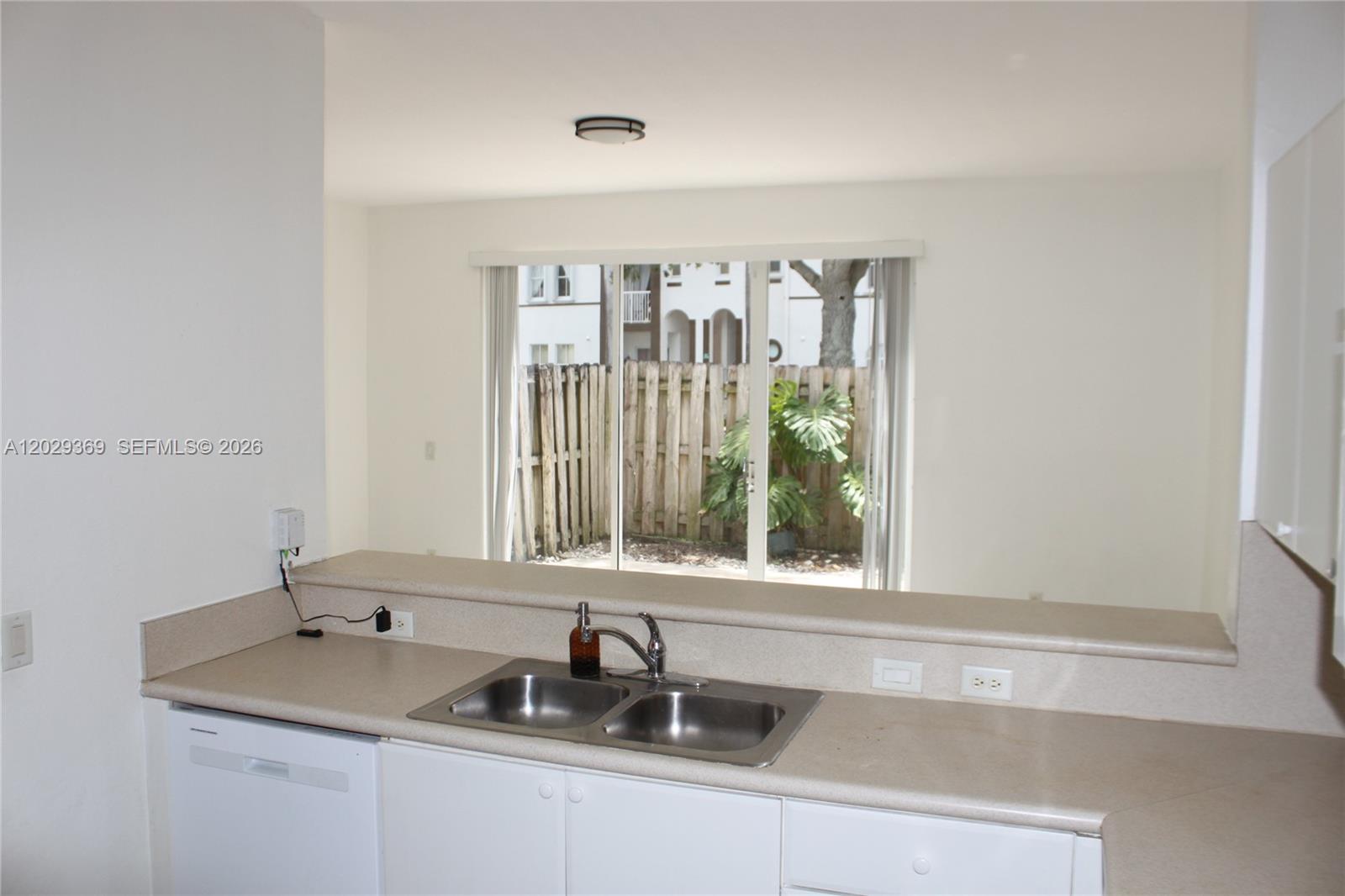 A kitchen sink and countertop overlook a living area with sliding glass doors to a patio — 4284 SW 157th Ave # 127, Miramar FL 33027, MIRAMAR, FL