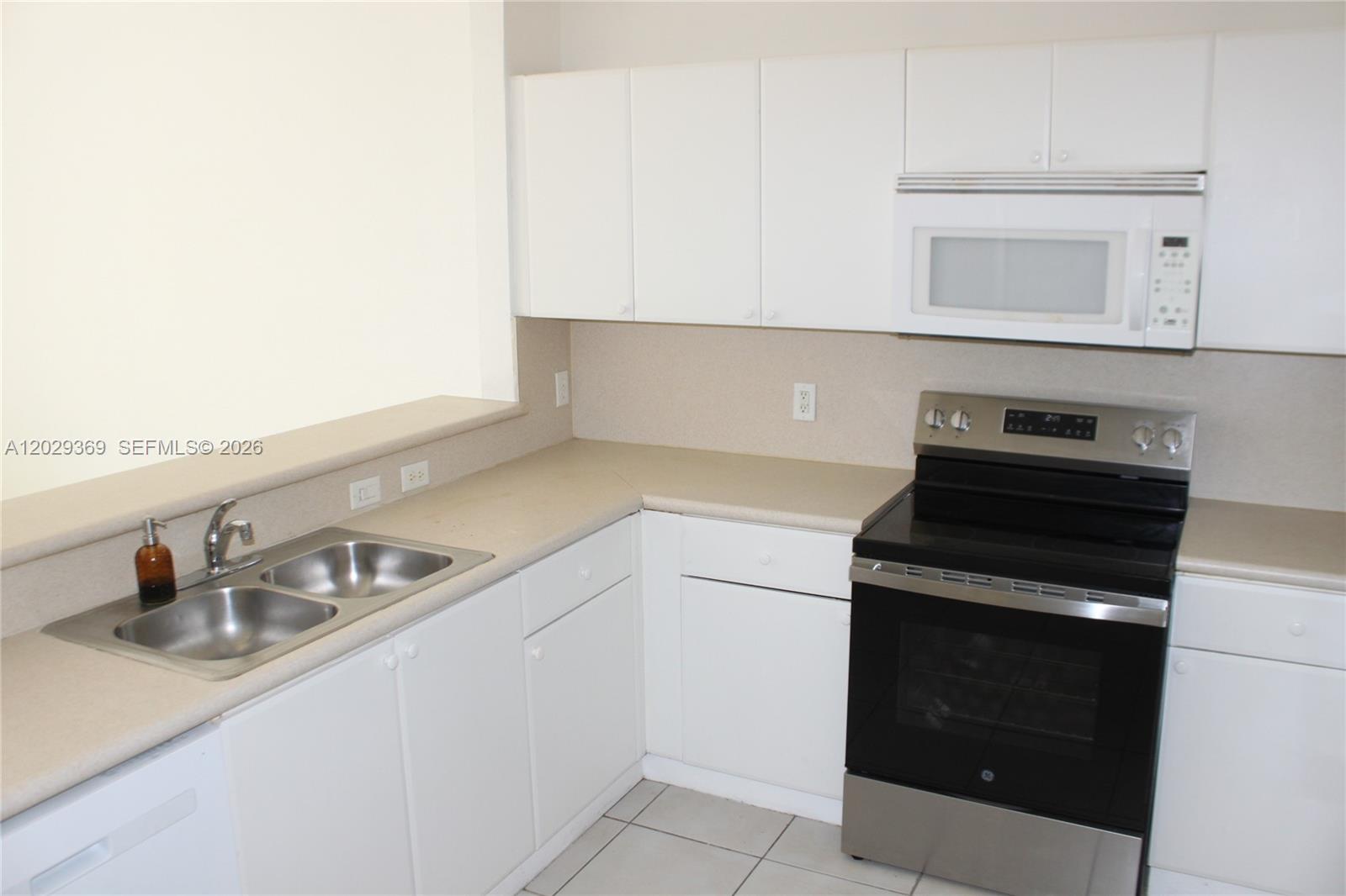 A kitchen features white cabinets, a stainless steel stove, a microwave, and a double sink — 4284 SW 157th Ave # 127, Miramar FL 33027, MIRAMAR, FL