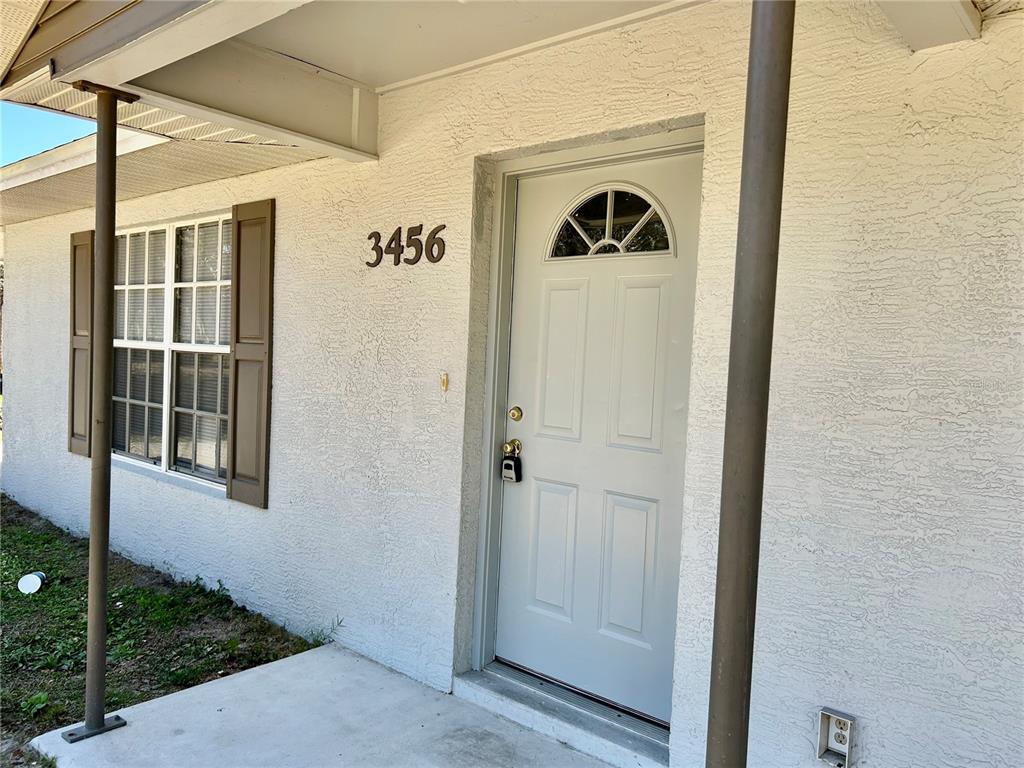 A light-colored exterior wall features a front door with a window and house numbers — 3456 ELM STREET, ZOLFO SPRINGS, FL