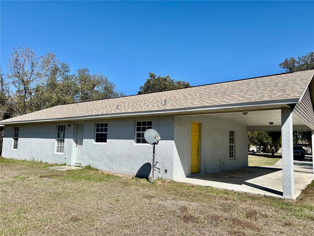 A single-story house with a gray stucco exterior, a yellow door, and an attached carport — 3456 ELM STREET, ZOLFO SPRINGS, FL