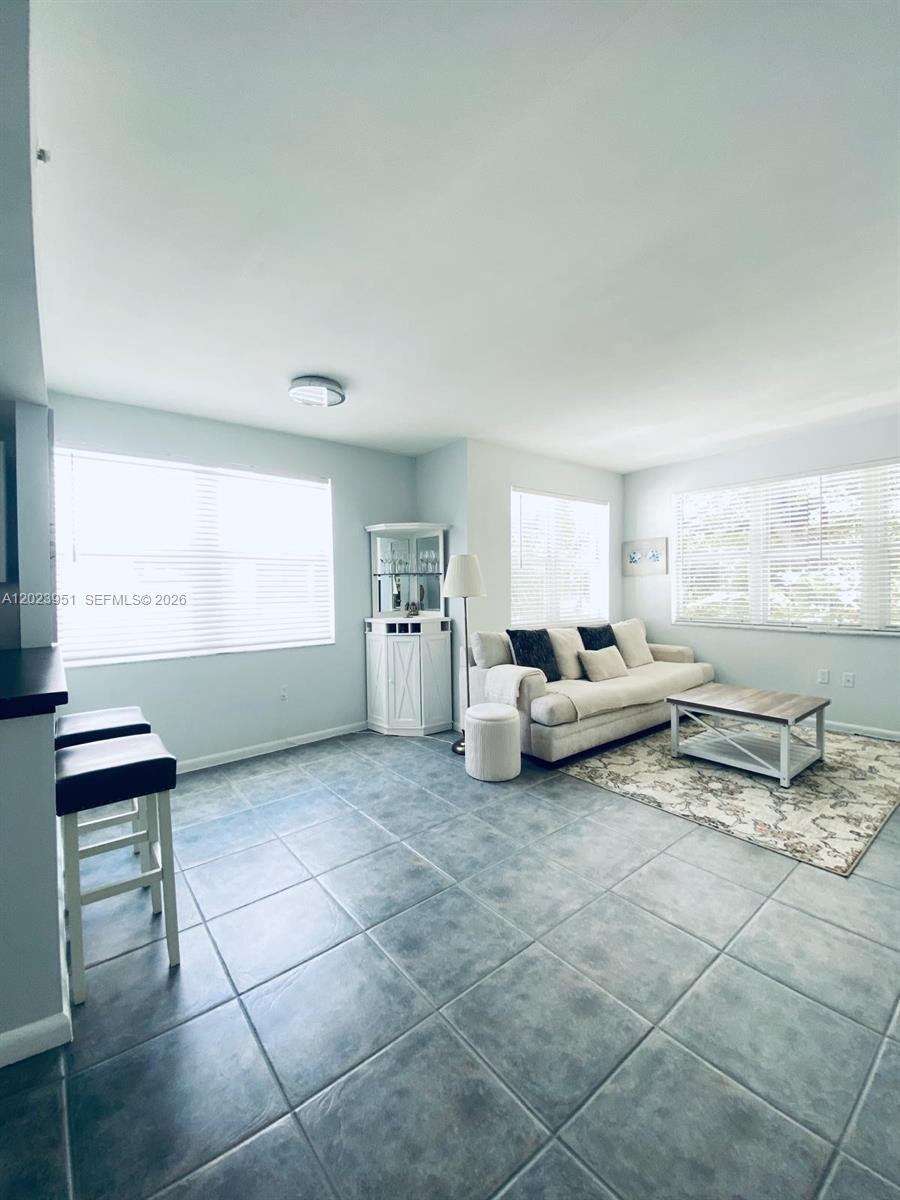 A living room features light gray tile floors, a beige sofa, and two large windows — 1550 Drexel Ave # 202, Miami Beach FL 33139, MIAMI BEACH, FL
