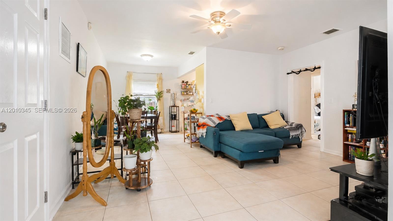 A living room features a blue sectional sofa, tile flooring, and a dining area beyond — 491 NW 108th Ter, Miami FL 33168, MIAMI, FL