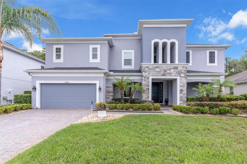 A two-story gray house with a stone facade, a two-car garage, and a landscaped lawn — 14067 JOMATT LOOP, WINTER GARDEN, FL
