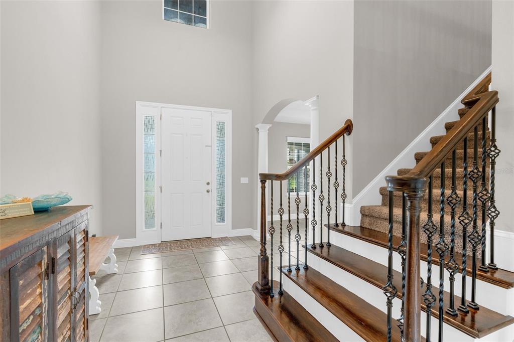 A two-story foyer features tiled flooring, a wooden staircase with iron railings, and a front door — 14067 JOMATT LOOP, WINTER GARDEN, FL