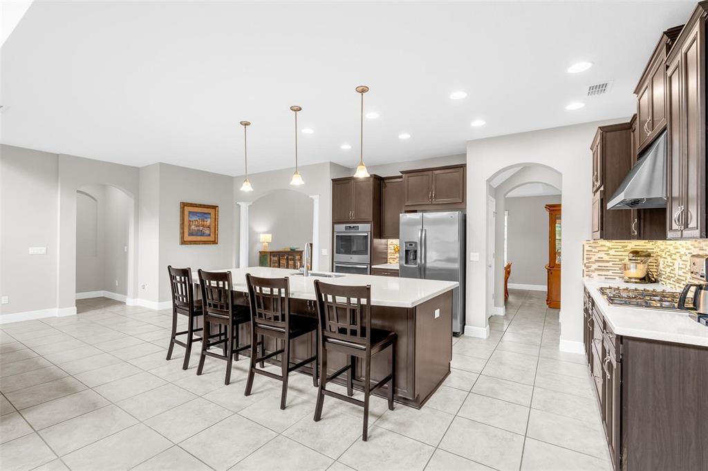 A kitchen features dark wood cabinetry, a large island with bar seating, and tile flooring — 14067 JOMATT LOOP, WINTER GARDEN, FL