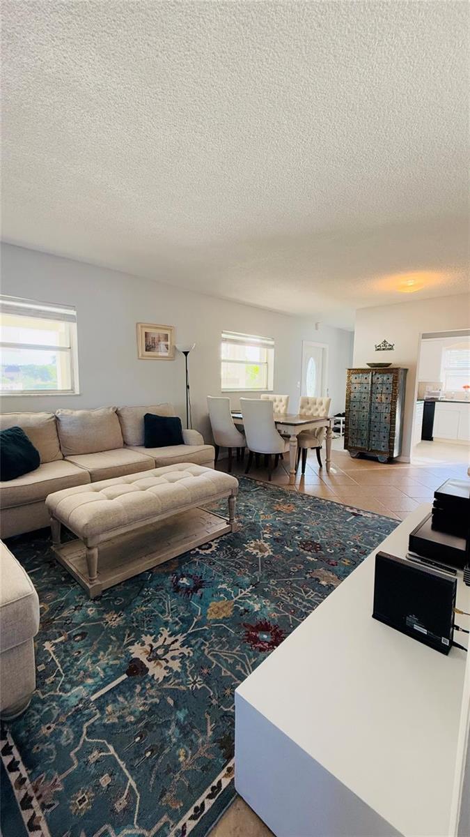 A living room with a beige sectional, tufted ottoman, and dining area on a patterned rug — 4200 Crystal Lake Drive # 210, Pompano Beach FL 33064, POMPANO BEACH, FL