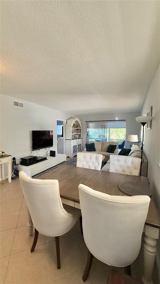 A dining area with white tufted chairs opens into a living room with a sofa — 4200 Crystal Lake Drive # 210, Pompano Beach FL 33064, POMPANO BEACH, FL