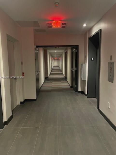 A hallway with gray tile flooring leads toward a long corridor with carpeted flooring — 151 SE 1ST # 1503, Miami FL 33131, MIAMI, FL