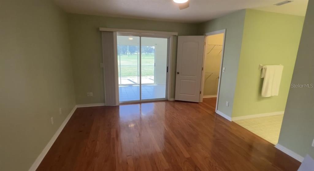 A bedroom with hardwood floors, a sliding glass door, and an attached walk-in closet — 6741 NORTHLAKE DRIVE, ZEPHYRHILLS, FL
