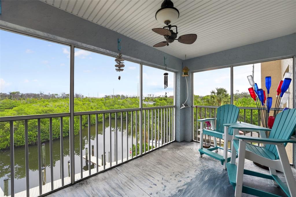 A screened-in balcony features two teal chairs, a ceiling fan, and a view of mangroves — 1960 OREGON TRAIL UNIT 2B, ENGLEWOOD, FL