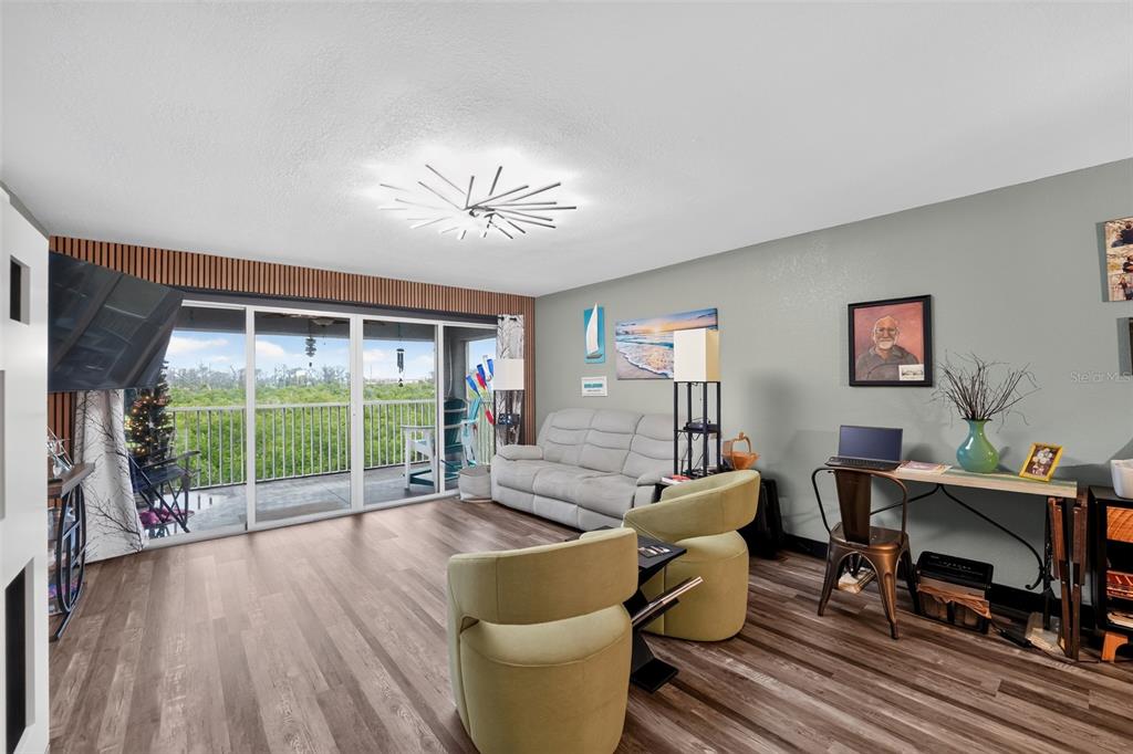 A living room features wood-look flooring, a light gray sofa, two armchairs, and a balcony view — 1960 OREGON TRAIL UNIT 2B, ENGLEWOOD, FL