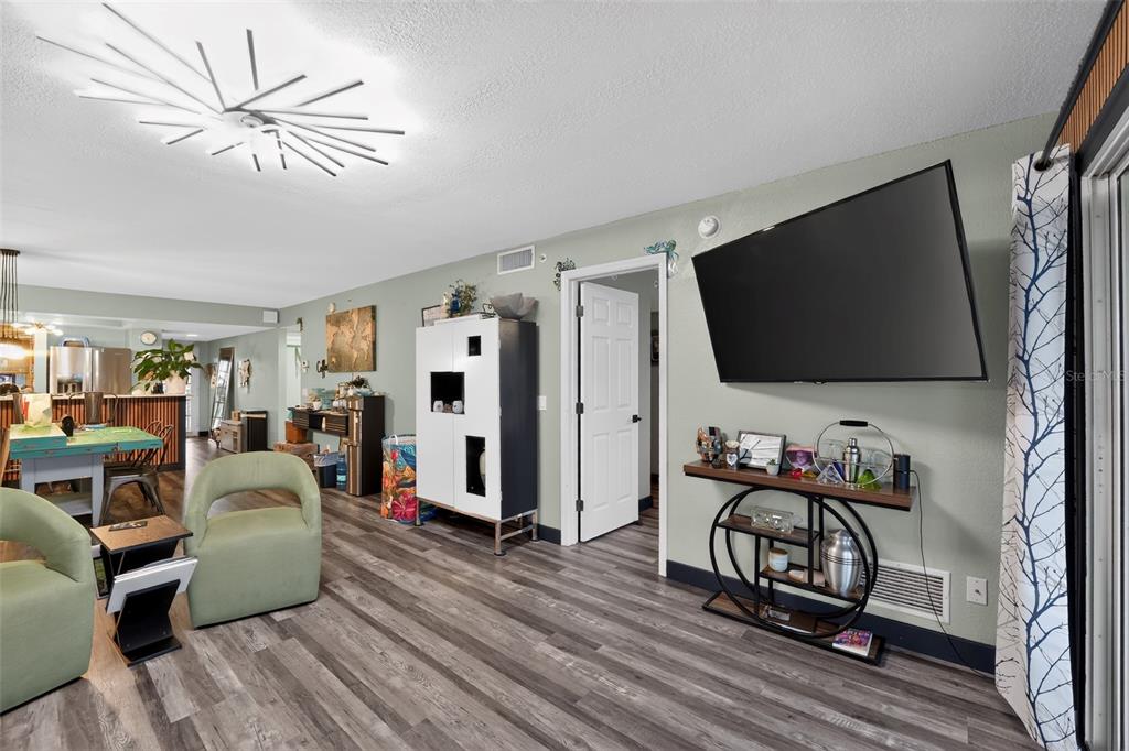 A living room with wood-look flooring, a wall-mounted television, and a modern starburst ceiling light — 1960 OREGON TRAIL UNIT 2B, ENGLEWOOD, FL