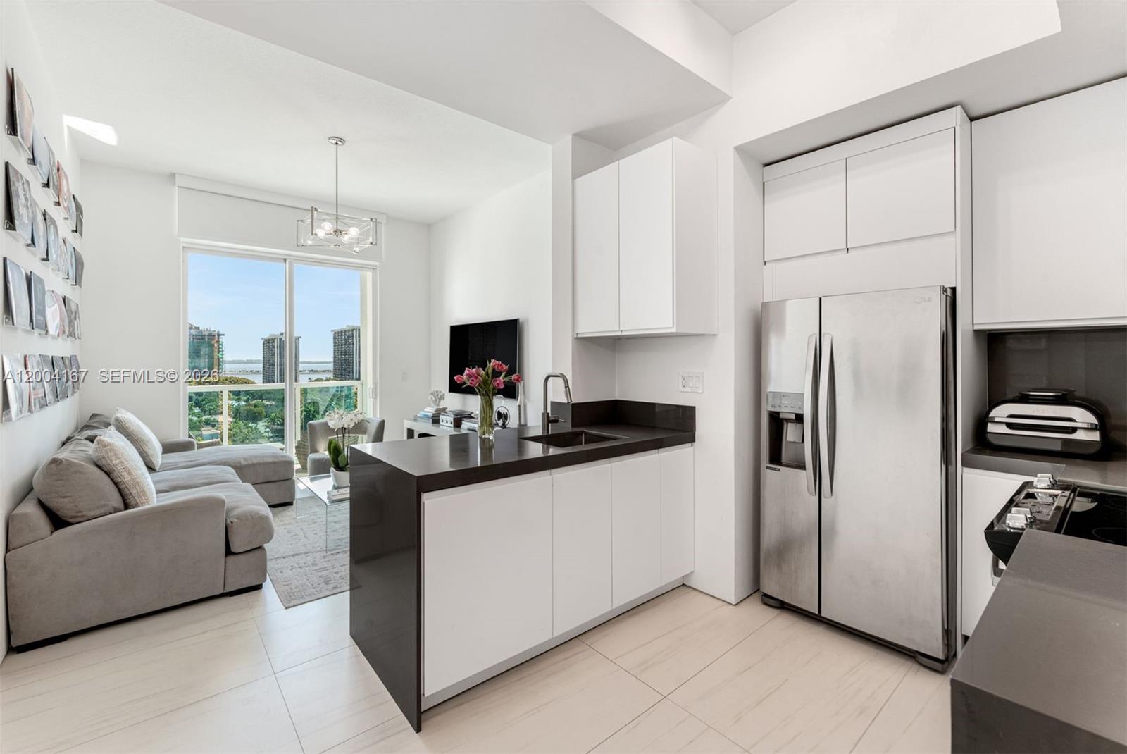 A modern kitchen with dark countertops and white cabinets opens into a living area — 1723 SW 2nd Ave, Miami FL 33129, MIAMI, FL