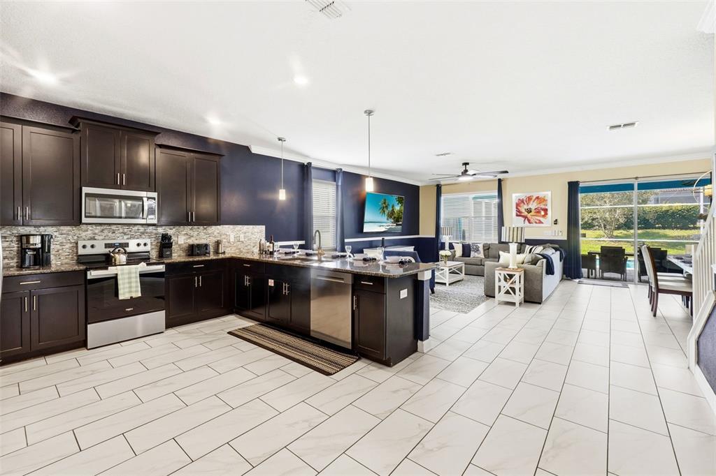 An open-concept kitchen and living area with dark cabinetry, stainless appliances, and white tile flooring — 9099 HAZARD STREET, DAVENPORT, FL