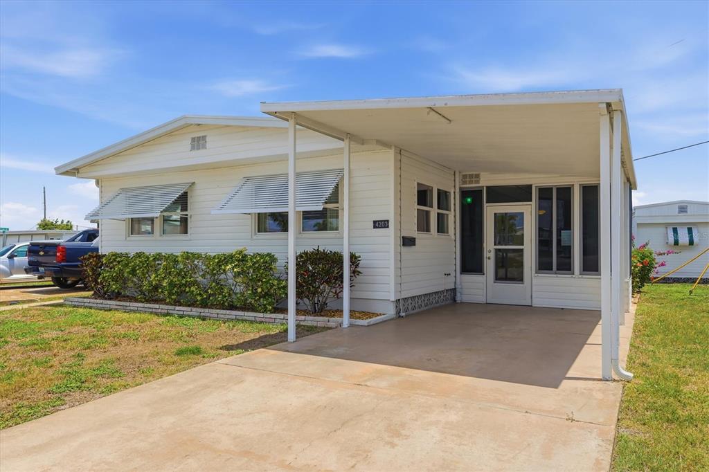 A white single-story manufactured home features a concrete driveway, a carport, and metal window awnings — 4203 11TH STREET COURT E, ELLENTON, FL